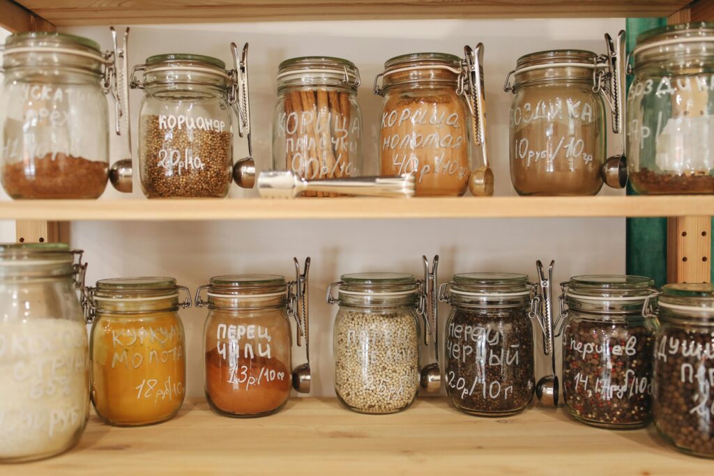 Organized pantry with glass jars holding a variety of spices and ingredients on wooden shelves.